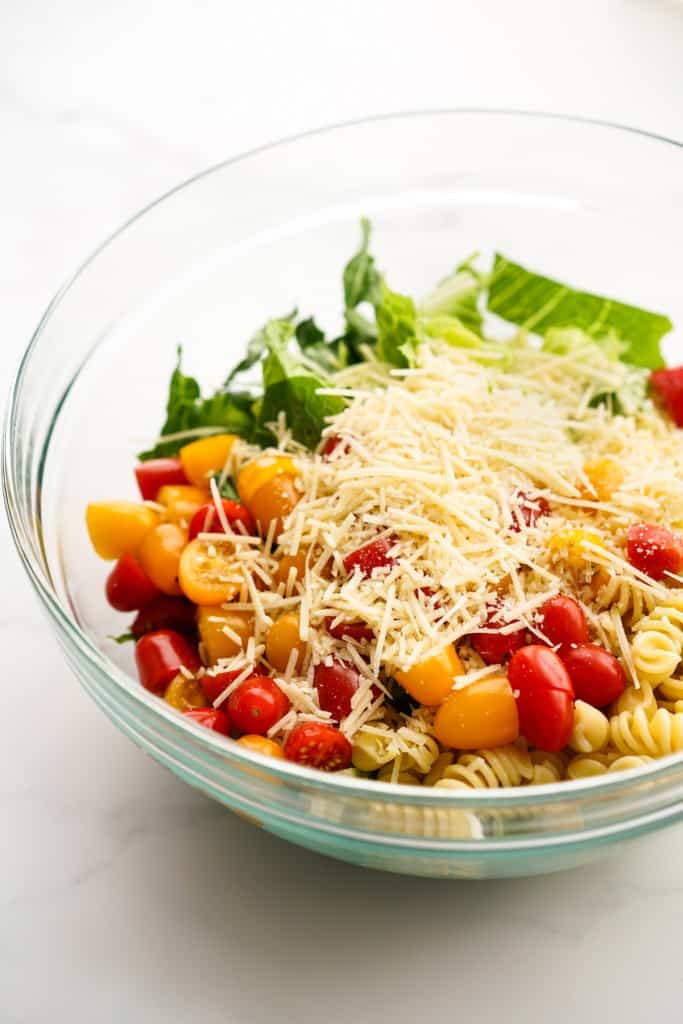 A bowl of romaine lettuce, cherry tomatoes, parmesan, rotini pasta
