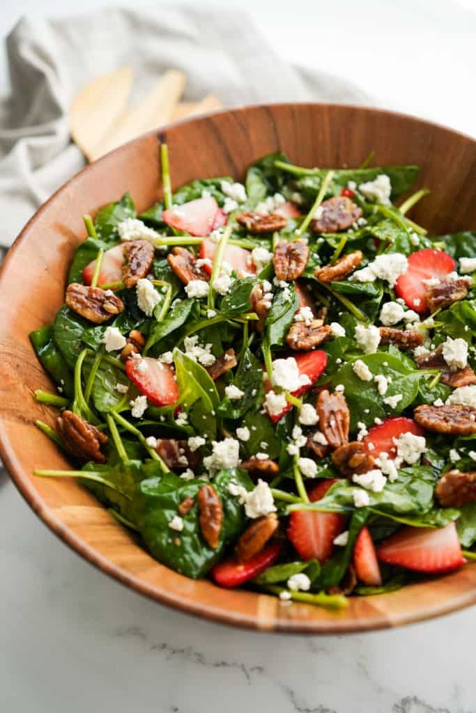 A wooden bowl loaded with spinach salad with strawberries, pecans and bacon