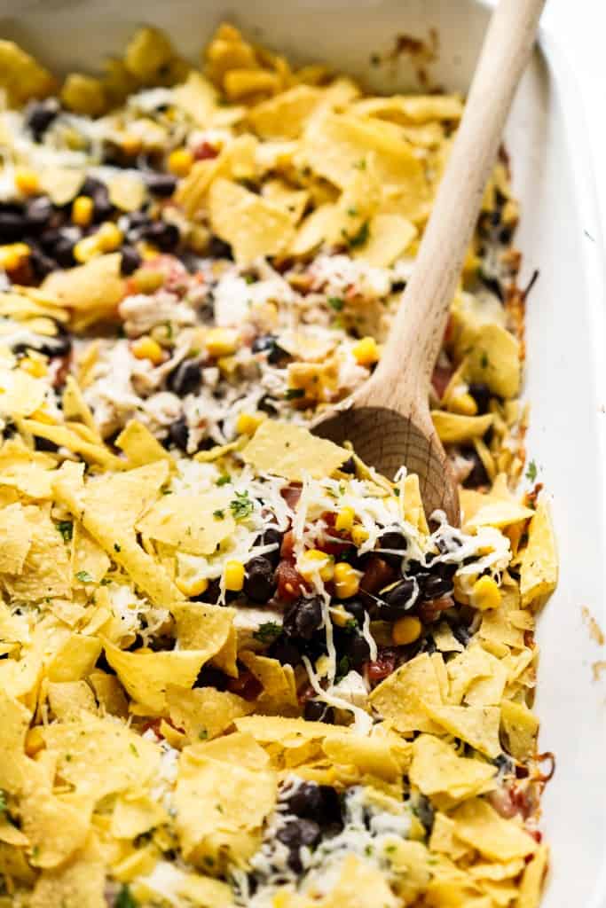 A wooden spoon in a Mexican casserole loaded with chicken, black beans and tortilla chips