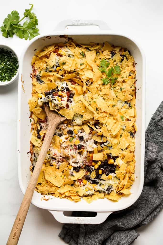 A rectangular casserole dish loaded with chicken, black beans, corn, cheese, tomatoes and topped with tortilla cheese