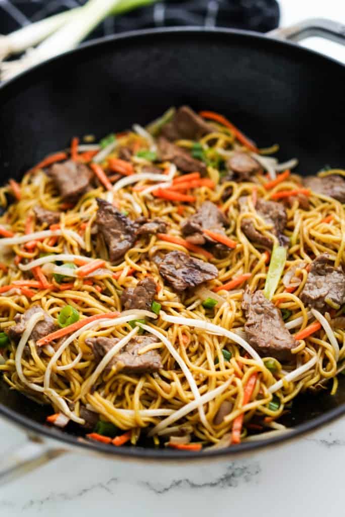 A wok loaded with beef chow mein, along with beans sprouts, green onions and matchstick carrots