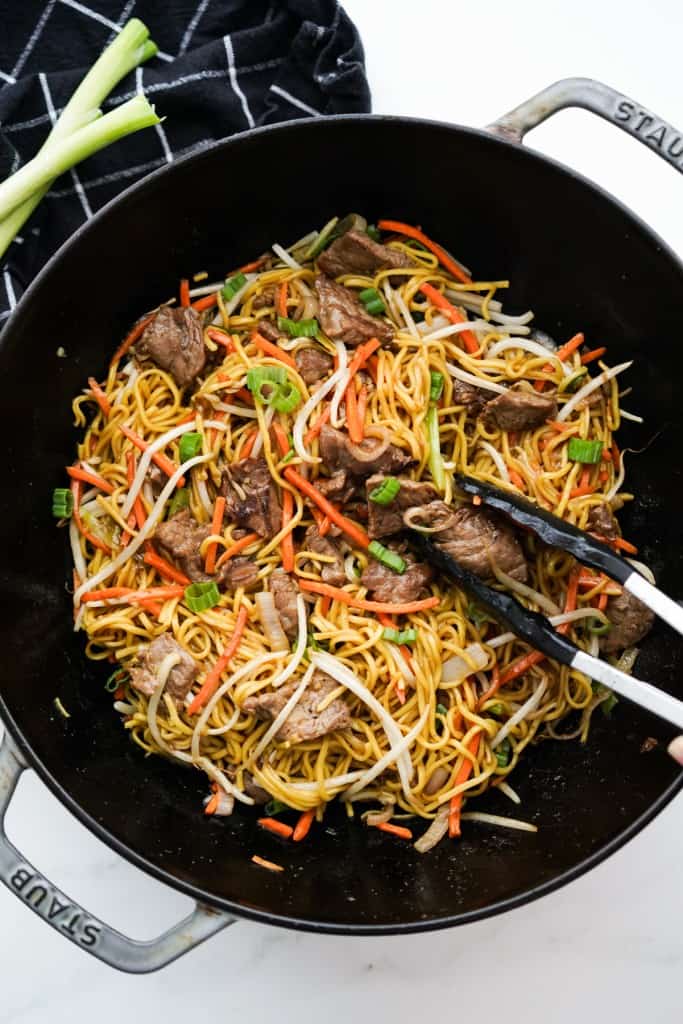 A large wok captured from the top down containing chow mein noodles, beef, and vegetables