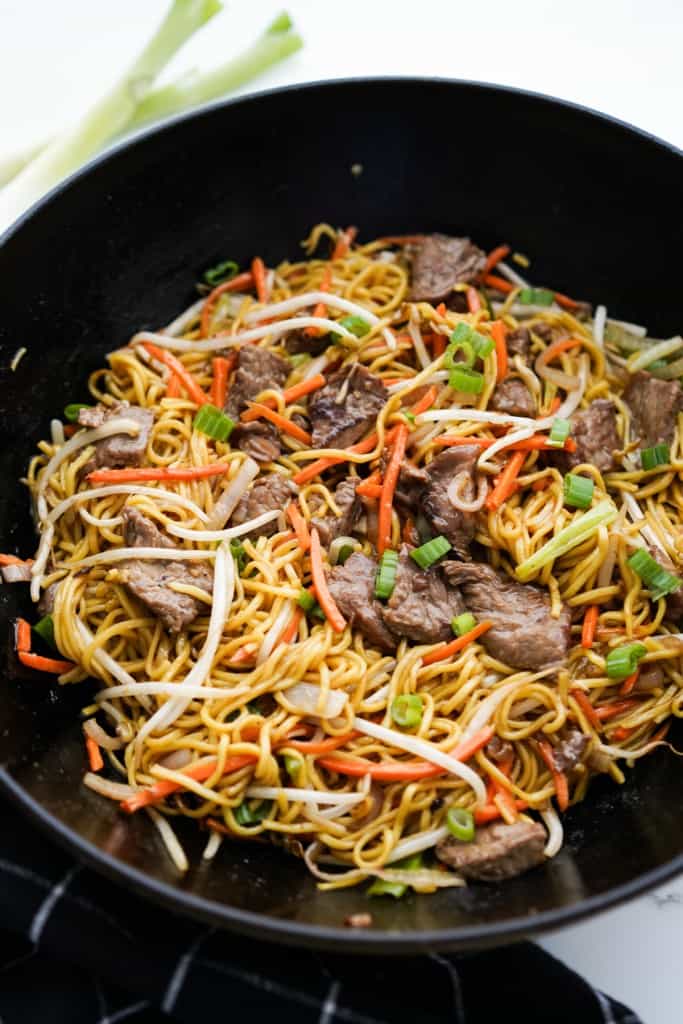 A wok loaded with beef chow mein topped with shredded carrots and bean sprouts
