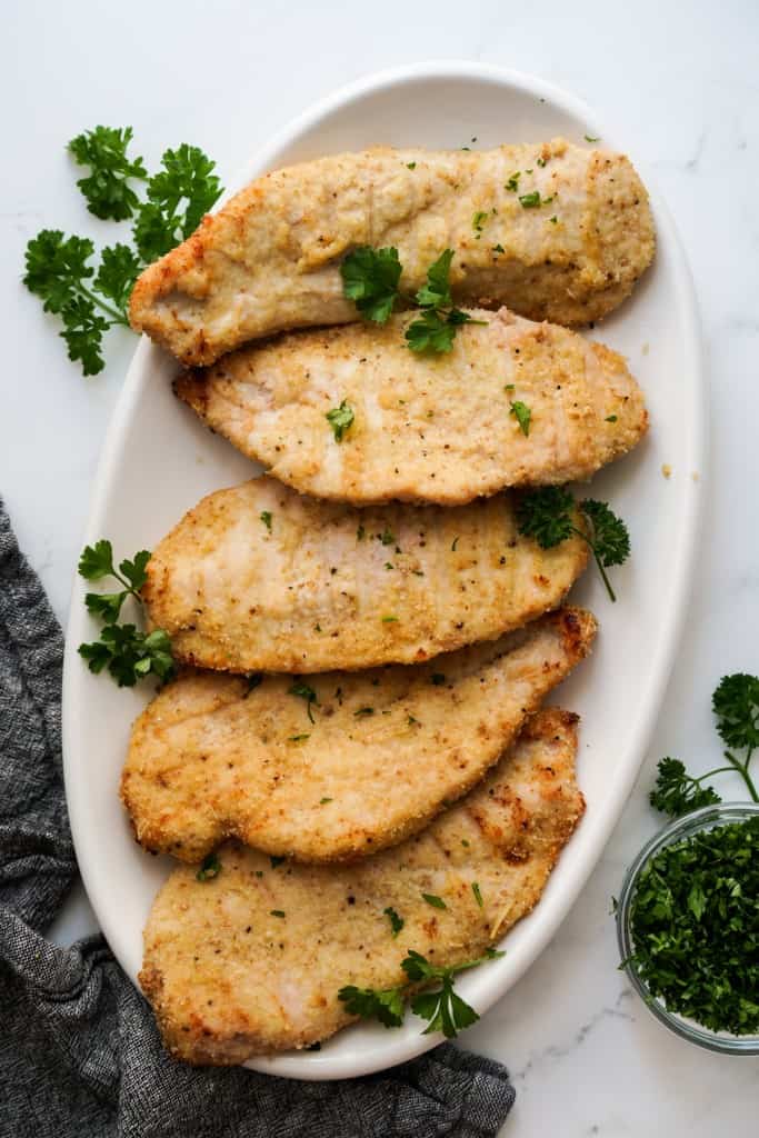 A platter of baked chicken cutlets that are lightly breaded
