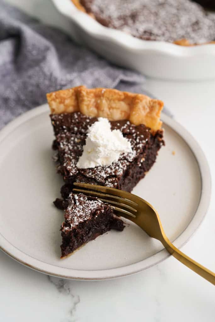 Slicing into a piece of chocolate chess pie topped with whipped cream