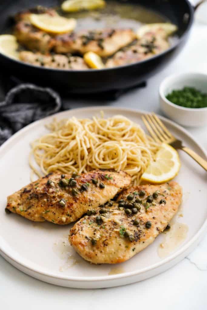 A plate of two sliced of chicken piccata served with spaghetti on the side