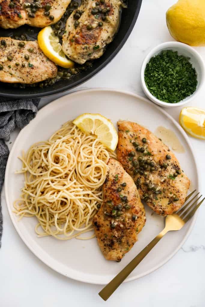A plate of spaghetti with two pieces of chicken piccata.