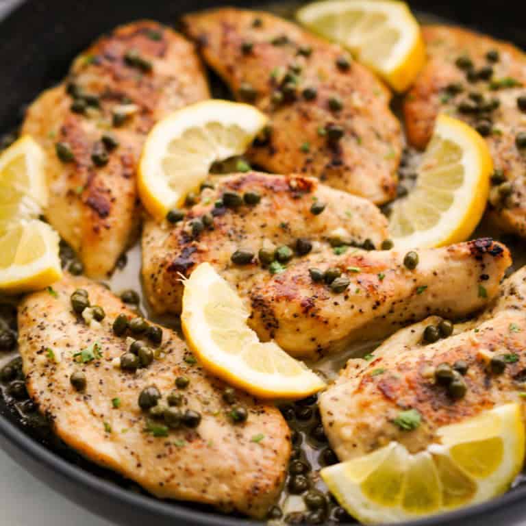 Lemon chicken piccata in a skillet topped with capers and lemon wedges
