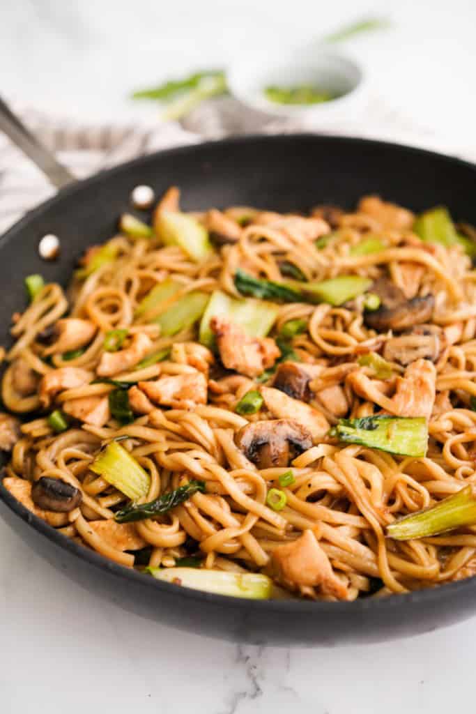 A large skillet of udon noodle stir fry with chicken