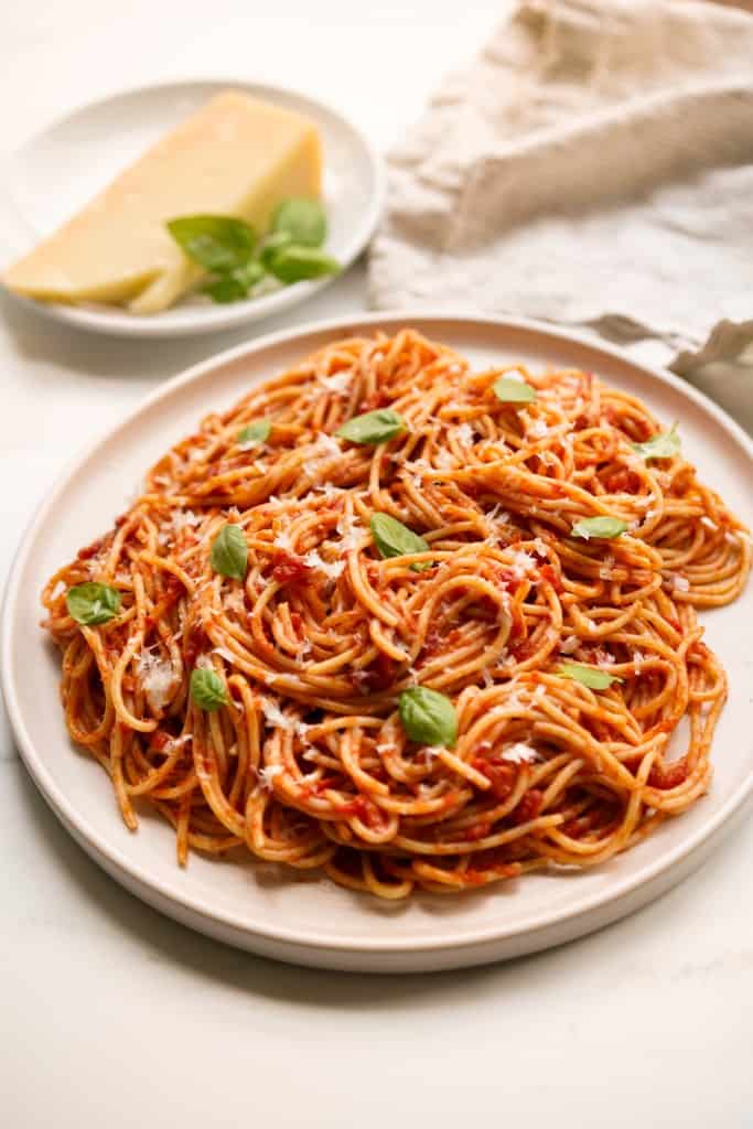 A large plate of pasta pomodoro tossed in tomato sauce and topped with parmesan and fresh basil