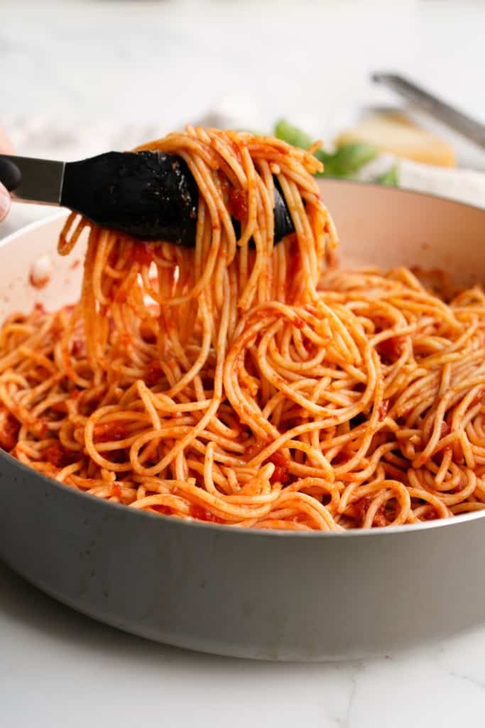 Lifting up spaghetti pasta tossed in pomodoro sauce in a large skillet