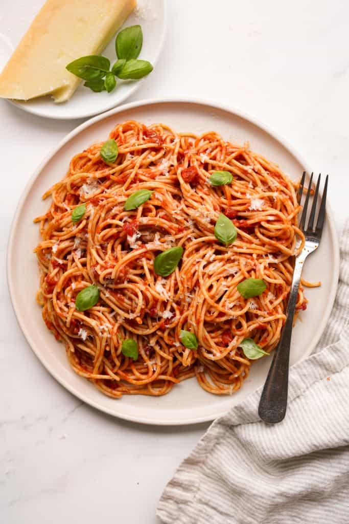 A plate of pasta pomodoro with parmesan cheese and fresh basil leaves in the background