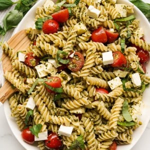 Closeup of fusilli pasta salad with grape tomatoes and cubed feta cheese tossed in a pesto sauce
