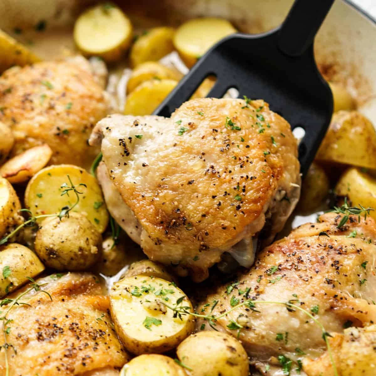 Lifting up a piece of chicken thighs with baby potatoes around it