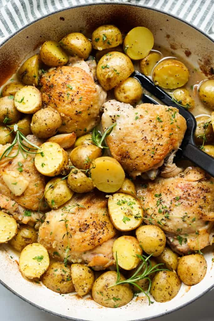 Top down close up view of a skillet loaded with halved baby potatoes and chicken thighs