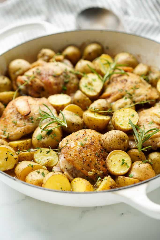 A skillet with chicken thighs nestle between lots of halved baby potatoes