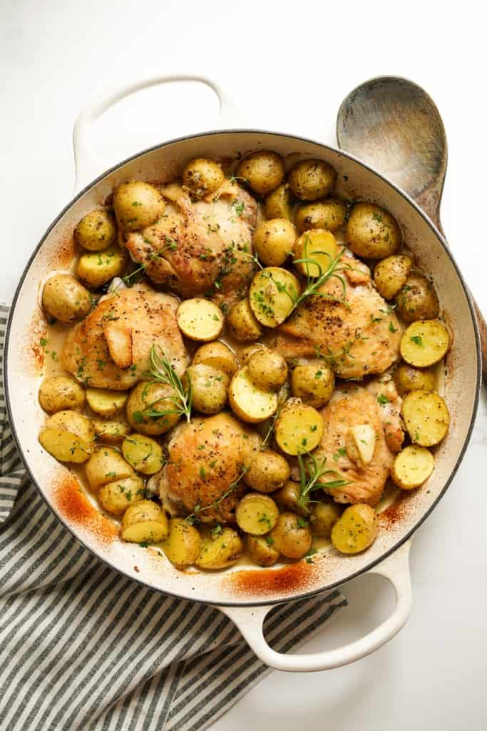 A large round skillet loaded with baked chicken thighs and potatoes