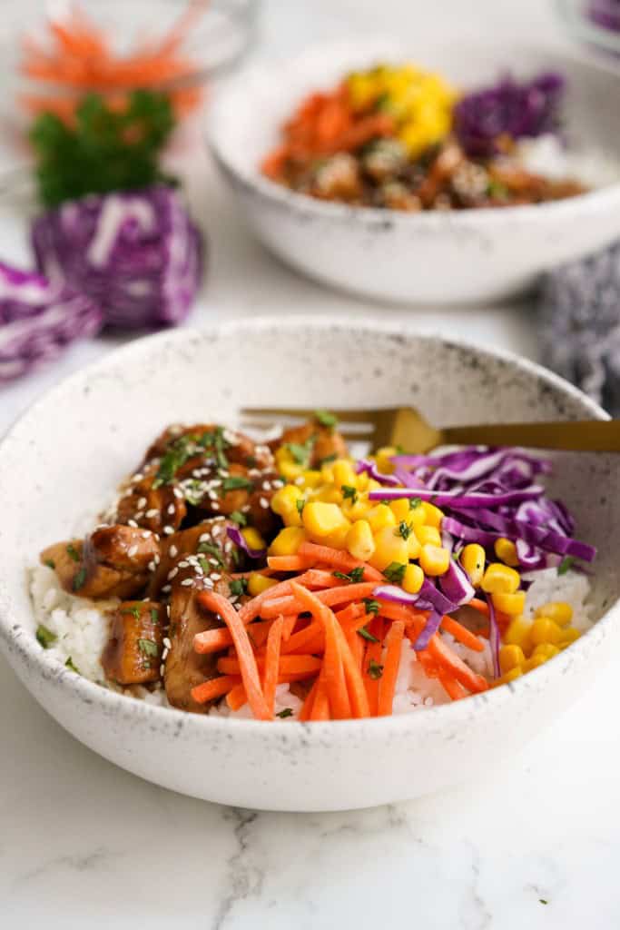 Rice topped with shredded carrots, corn, cabbage, soy glazed chicken