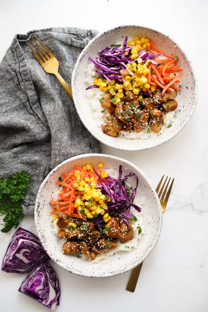 Two bowls of rice topped with soy glazed chicken and veggies, with forks on the side