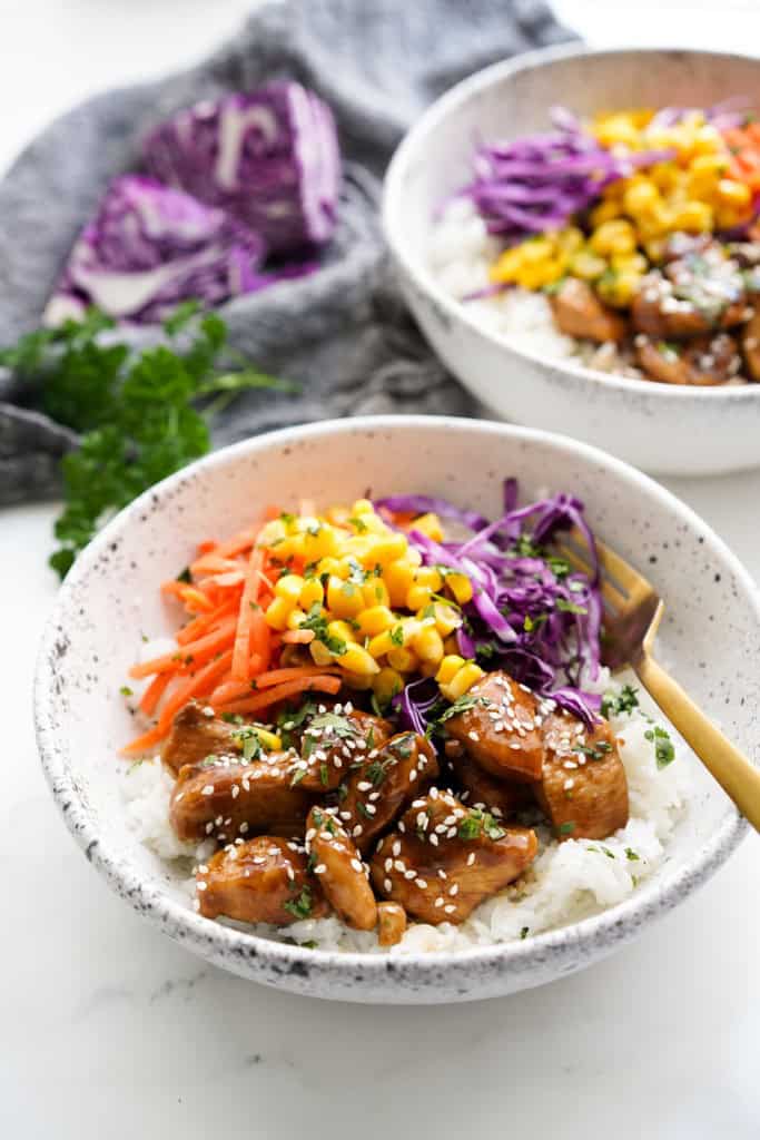 Two bowls of chicken rice bowl along with veggies