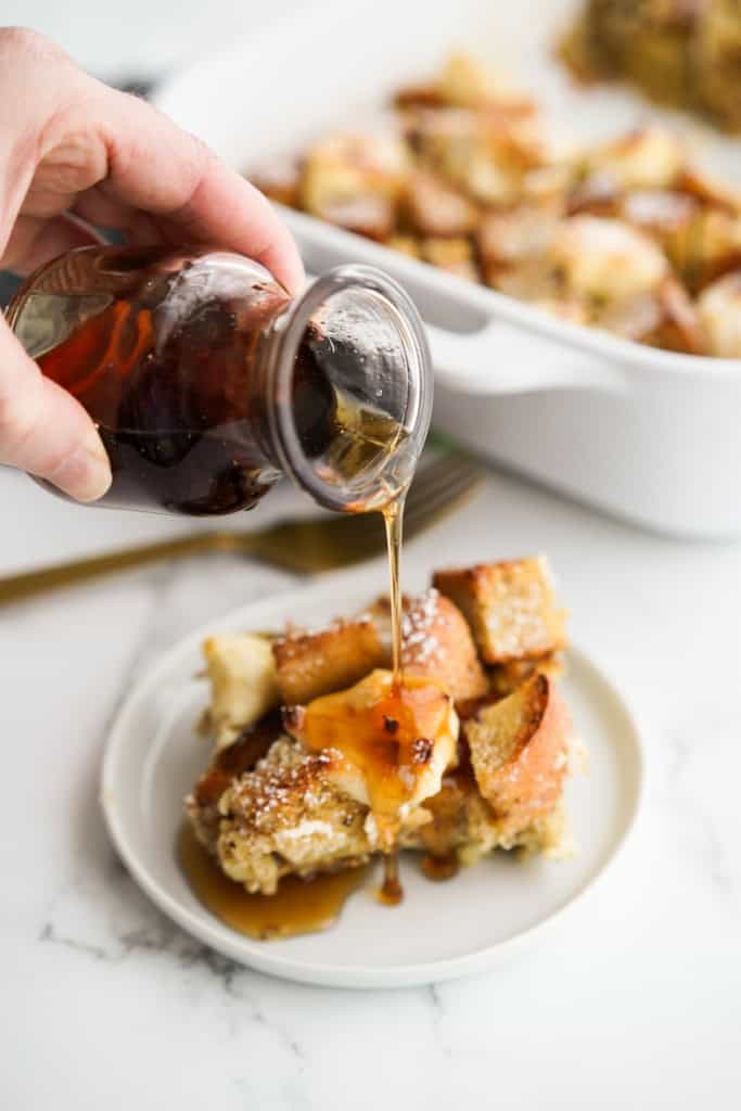 Pouring maple syrup onto a slice of French toast casserole with cream cheese