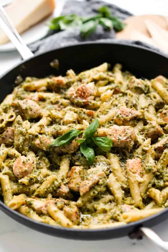 A large skillet of penne pasta with chicken and creamy pesto sauce