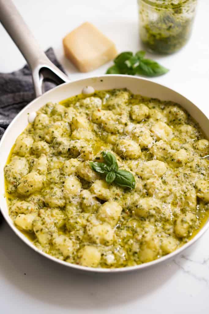 A skillet loaded with soft potato gnocchi in creamy pesto sauce