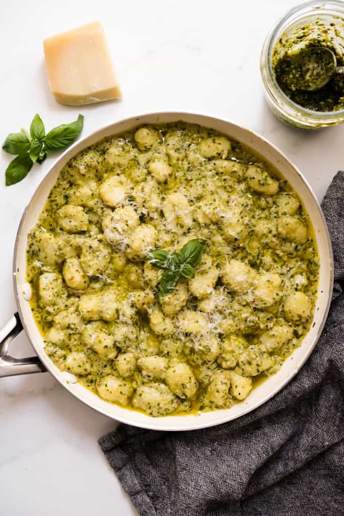 A skillet filled with potato gnocchi coated in creamy basil pesto sauce