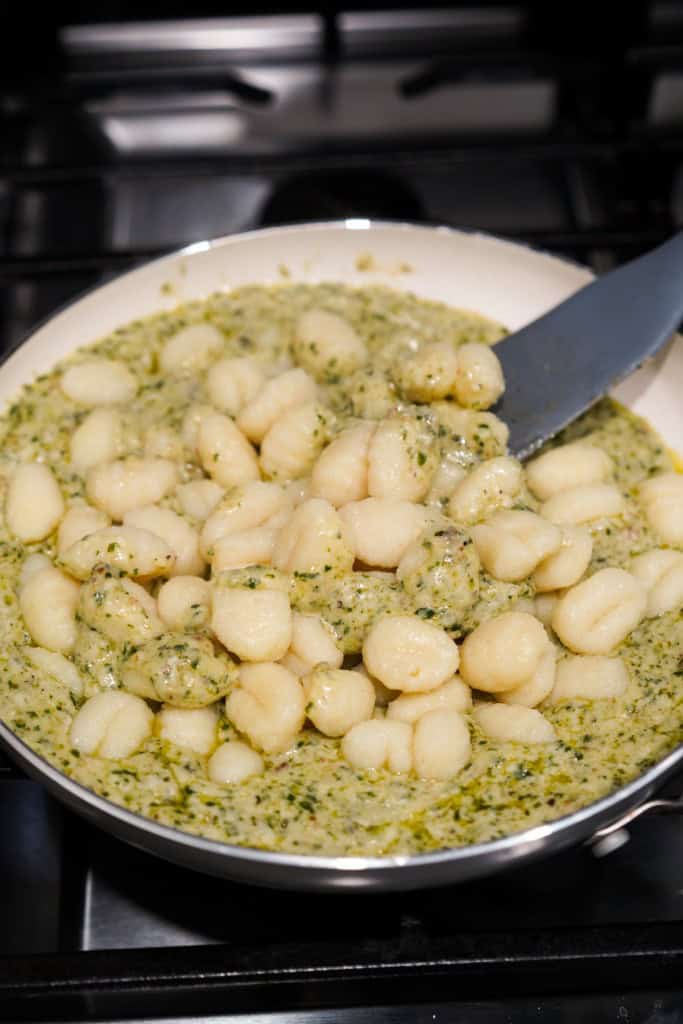 Coating gnocchi pasta in creamy pesto sauce