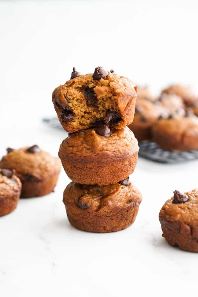 Three pumpkin chocolate chip muffins stacked on top of each other, the top one is being bitten into